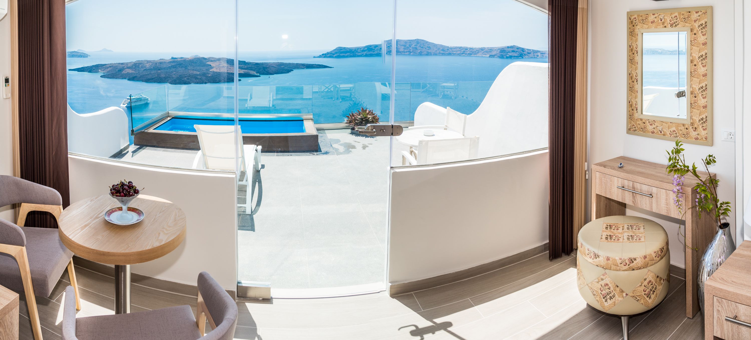 Un balcón con puerta de cristal, piscina, mobiliario blanco y vistas al mar y a las islas.