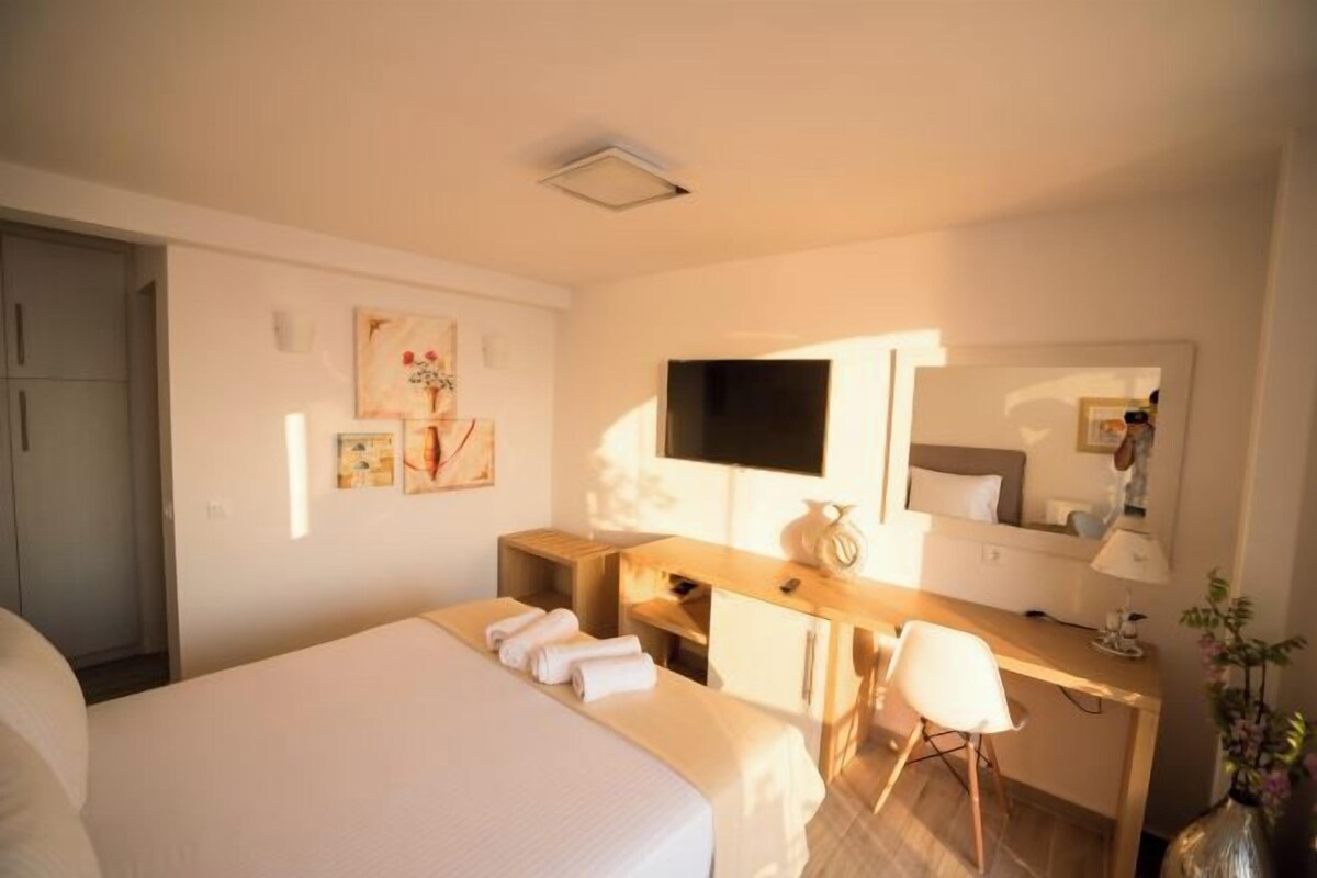 Ein Hotelzimmer mit einem großen Bett, einem Schreibtisch mit Stuhl, einem Flachbildfernseher, einem Spiegel und Bildern an den Wänden.