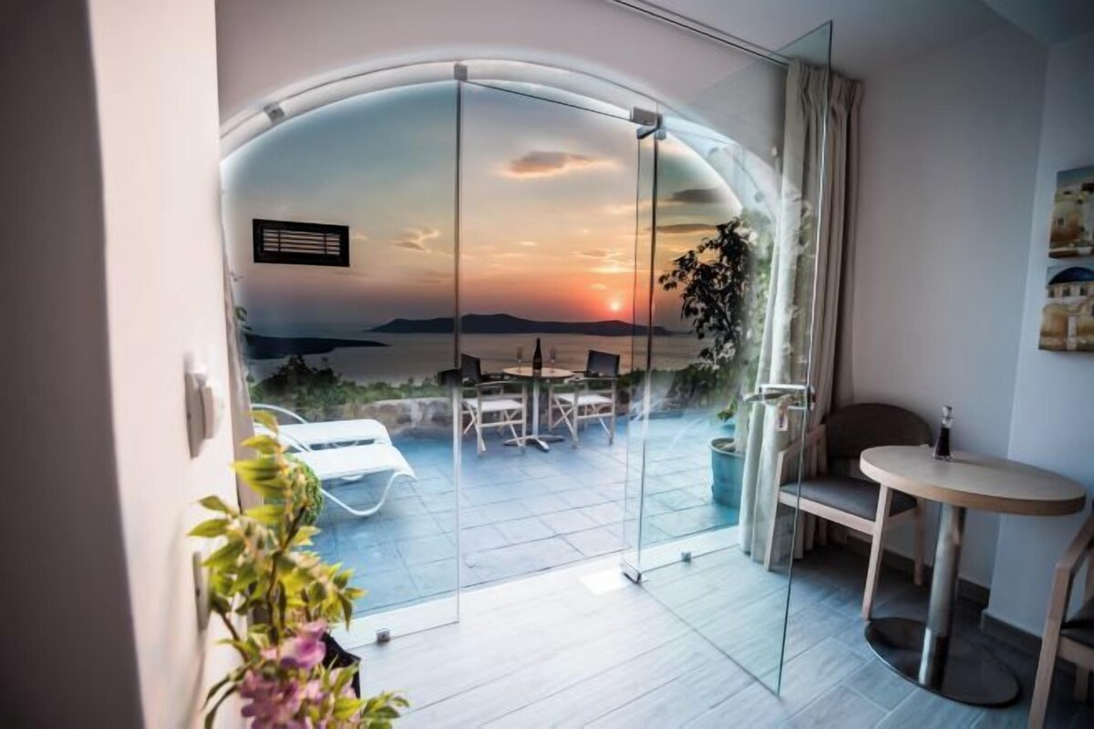 Ein modernes Zimmer mit Glastür, die auf einen Außenbereich mit Tisch und Stühlen, einem kleinen runden Tisch und einem Blumentopf führt.