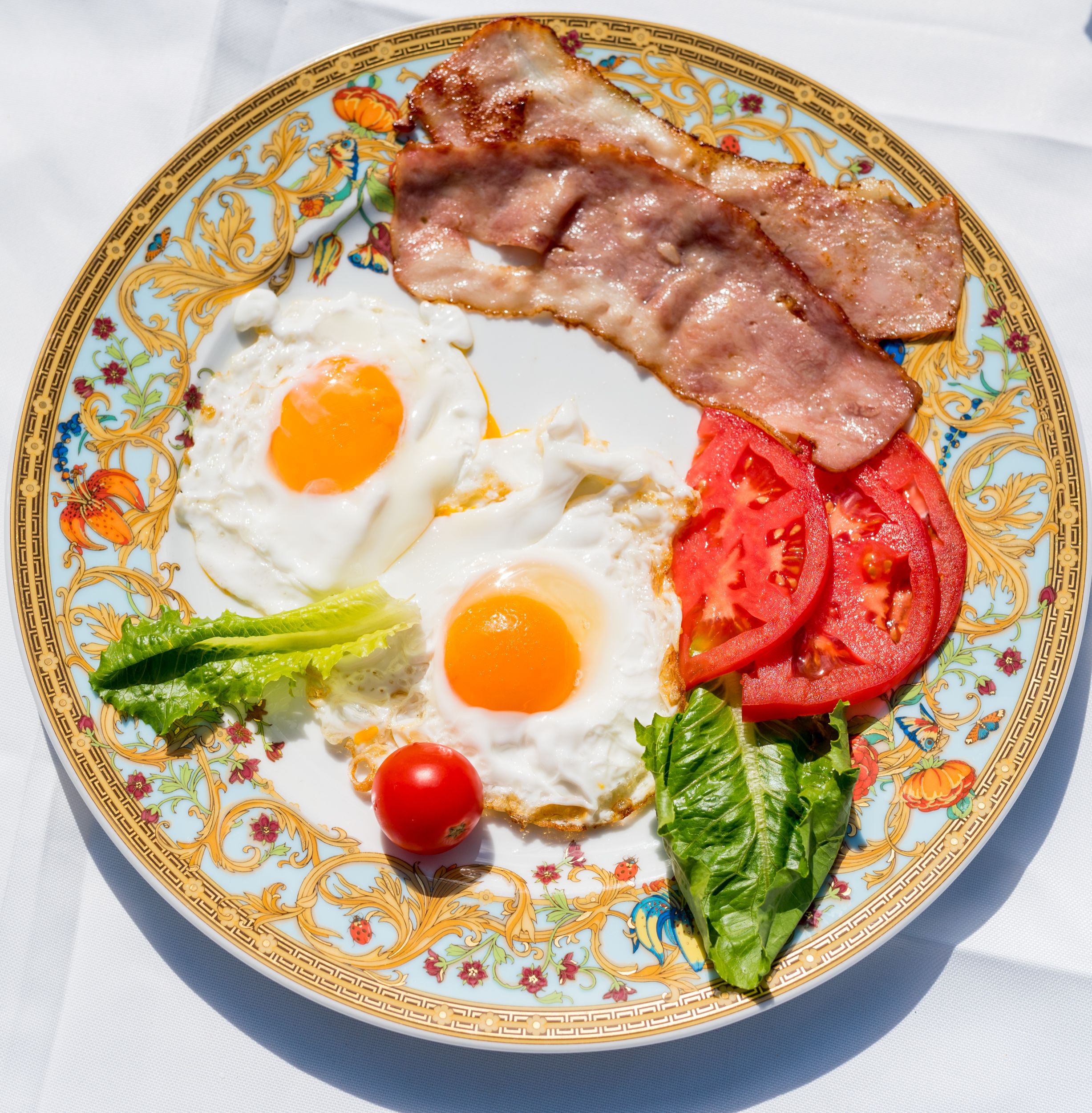 A plate with eggs, bacon, tomatoes, lettuce, and a cherry tomato.