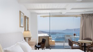 A hotel room with a large bed, a desk, and a balcony with a view of the sea. - Kratiras View Luxury Suites (Santorini)
