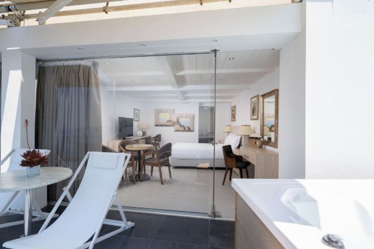 Ein modernes Hotelzimmer mit Glastür zu einem Balkon, einem Bett, einem Schreibtisch und einem Badezimmer mit einer Badewanne.