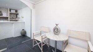 A small, modern room with a round table, two wicker chairs, a decorative vase, and a white cabinet with shelves. - Kratiras View Luxury Suites (Santorini)