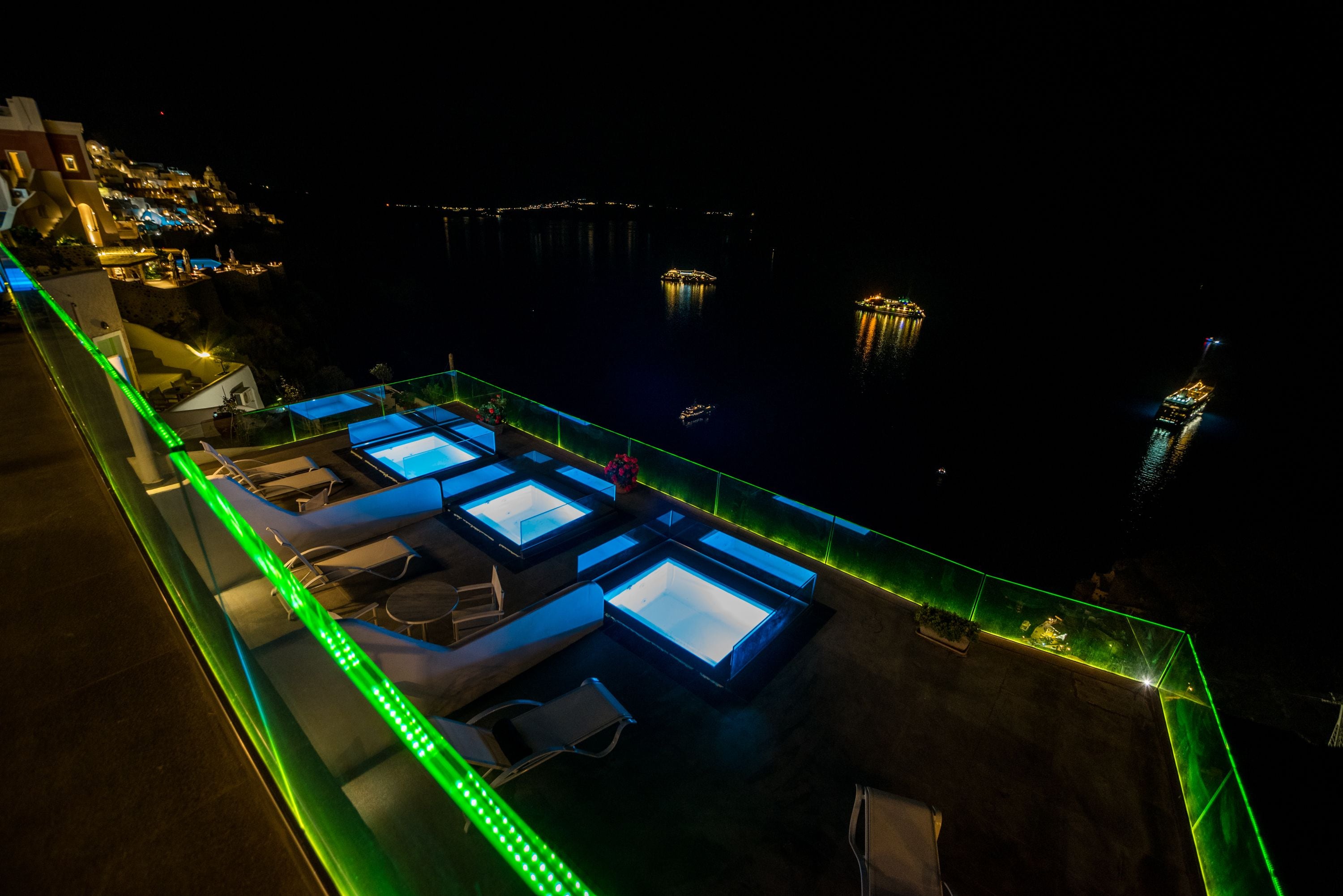 A rooftop terrace with multiple sun loungers and a pool area, surrounded by a railing with green lighting.