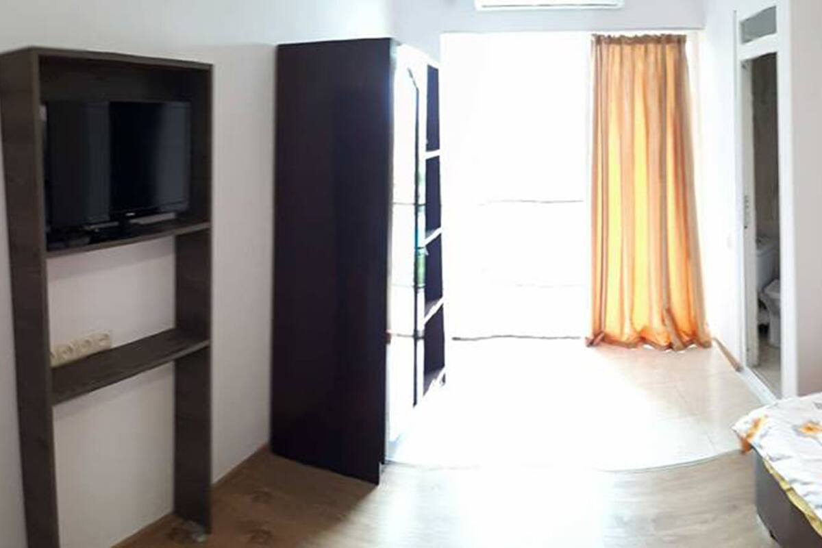 A room with two single beds, a TV on the left, and a large window with curtains.