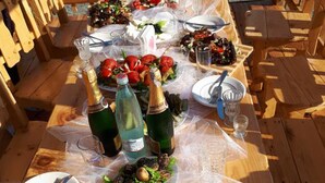Una terraza de madera con una mesa lista para una comida, que incluye platos, cubiertos y botellas de agua y champán.