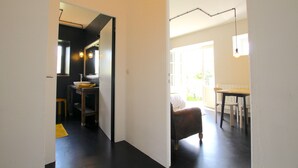 A hallway leading to a dining area with a table and chairs, a bench, and a kitchen area with a sink and counter. - La Maison Folia (Quettreville-sur-Sienne)