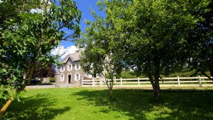 A grassy area with a stone building and a white fence. - La Maison Folia (Quettreville-sur-Sienne)