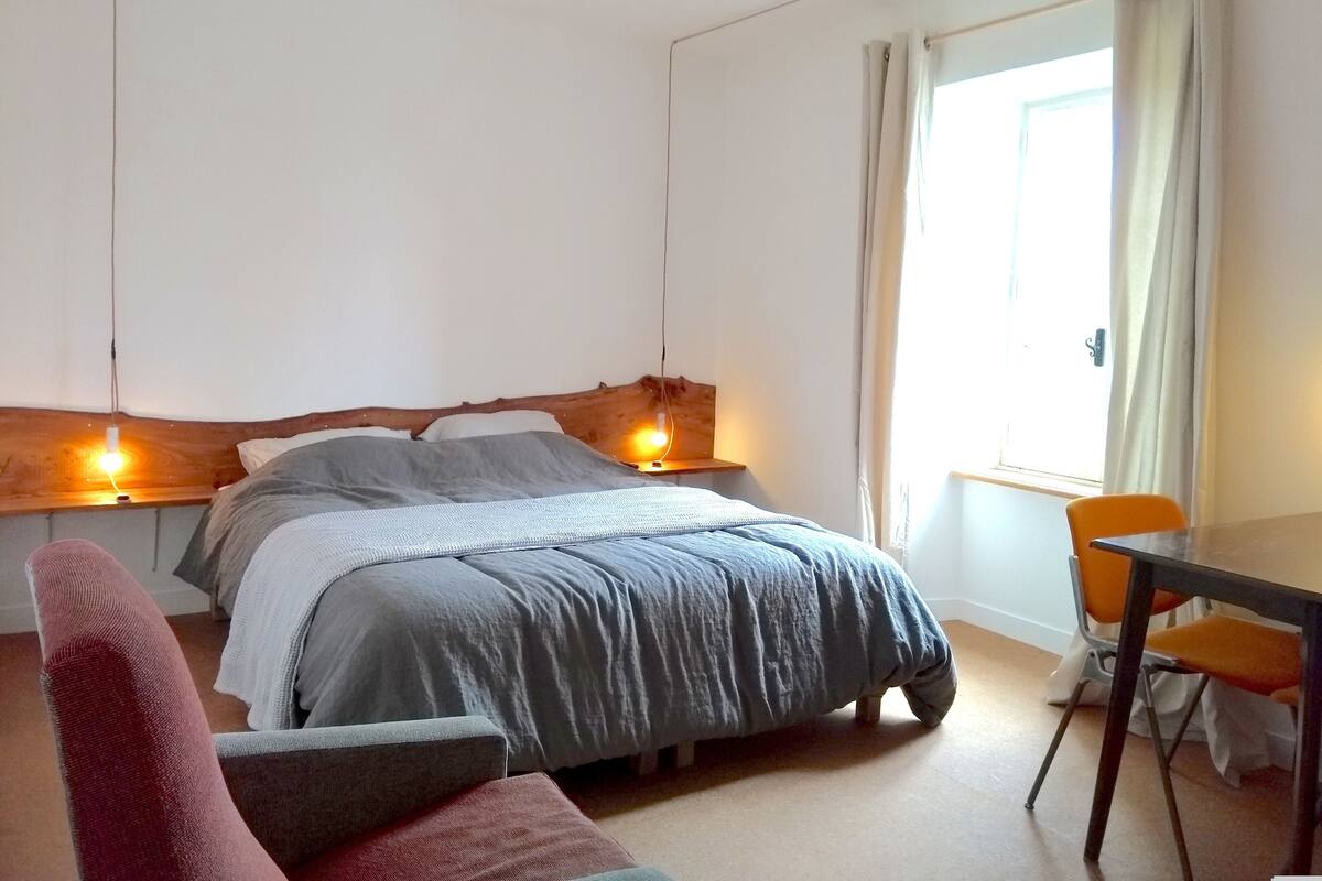 A bedroom with a bed, bedside lamps, a chair, and a table.