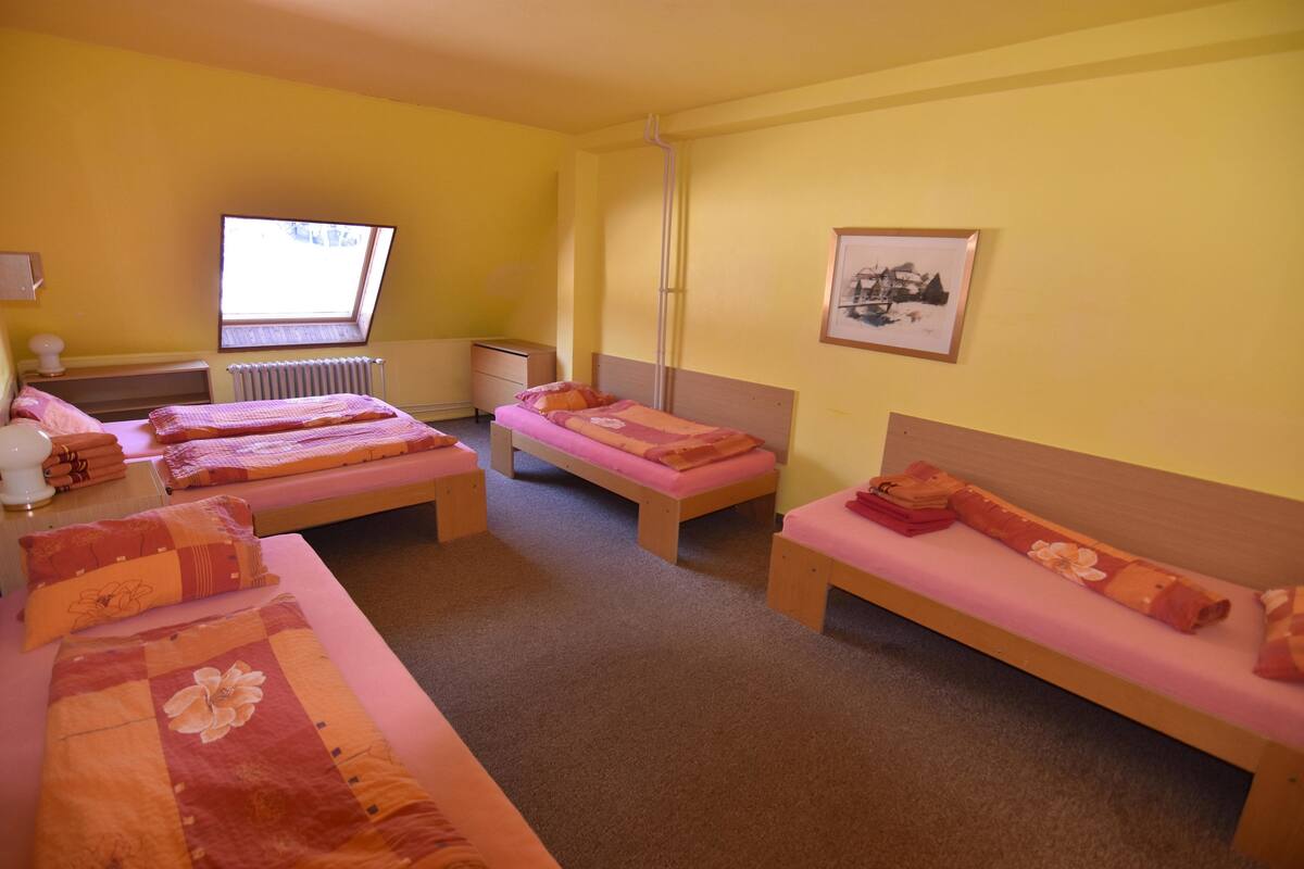 A room with three single beds, a radiator, a window, and a framed picture on the wall.