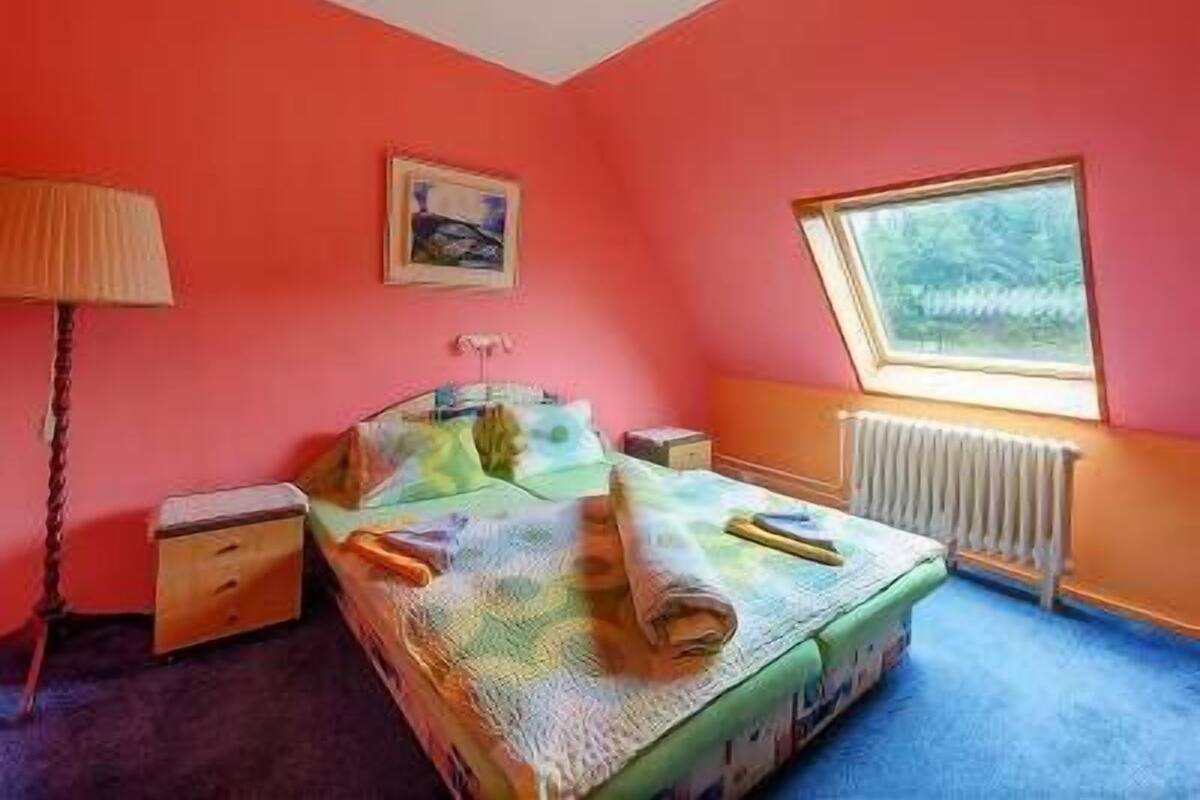 A bedroom with a bed, a window, a radiator, and a painting on the wall.