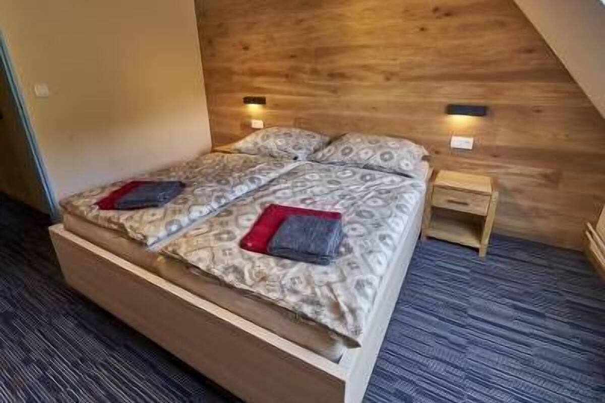A bedroom with a wooden headboard, a double bed with patterned bedding, two bedside tables, and a small nightstand.