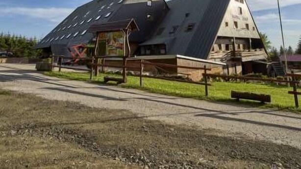 Un edificio con techo inclinado y una estructura adosada con terraza de madera.