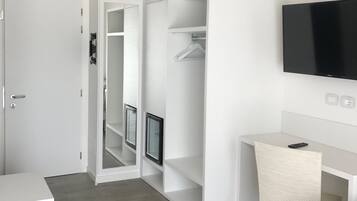 Une chambre d’hôtel moderne dotée d’un dressing, d’un téléviseur à écran plat fixé au mur, d’un petit bureau avec une chaise et d’un plancher en bois gris.