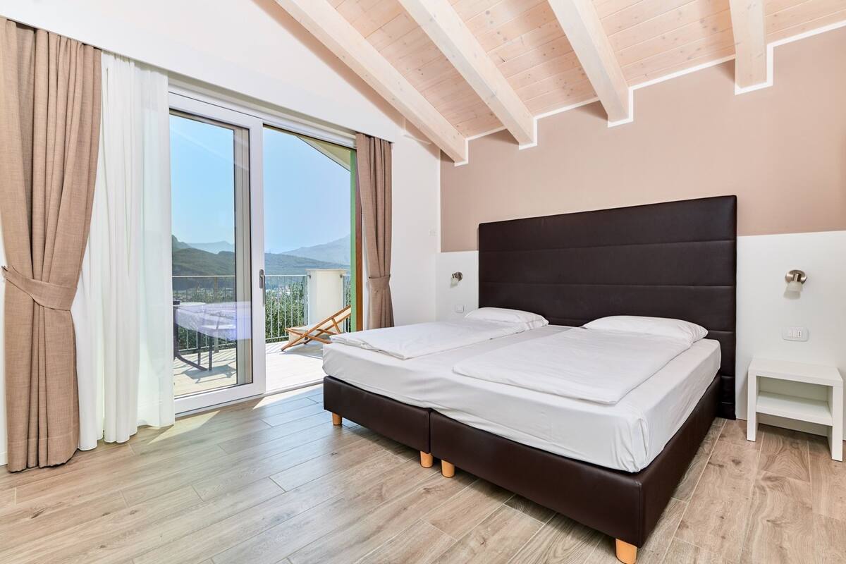 A bedroom with a large bed, a small bedside table, and a view of the outdoors through a sliding glass door.