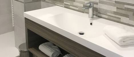 A modern bathroom with a large mirror, a white sink, and a shower area.