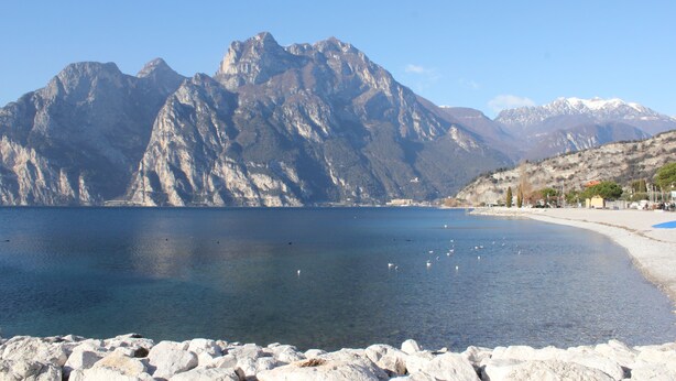 Un lac avec des montagnes en arrière-plan, une rive rocheuse et quelques bâtiments situés sur la rive opposée.