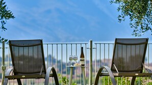 Deux chaises placées à l’extérieur, avec une table entre elles, une bouteille de vin et deux verres posés sur la table.