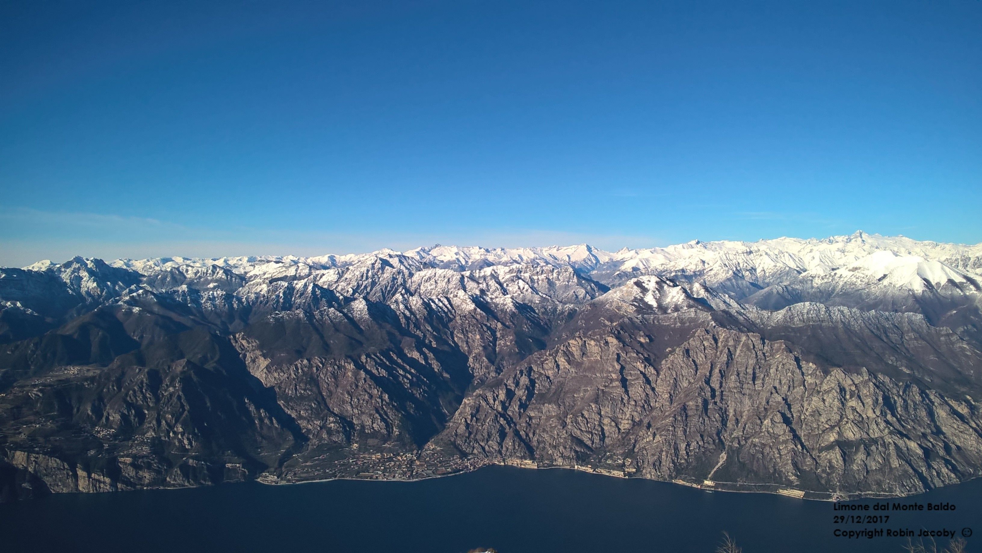 Un paysage montagneux aux sommets enneigés, avec une ville côtière en contrebas.
