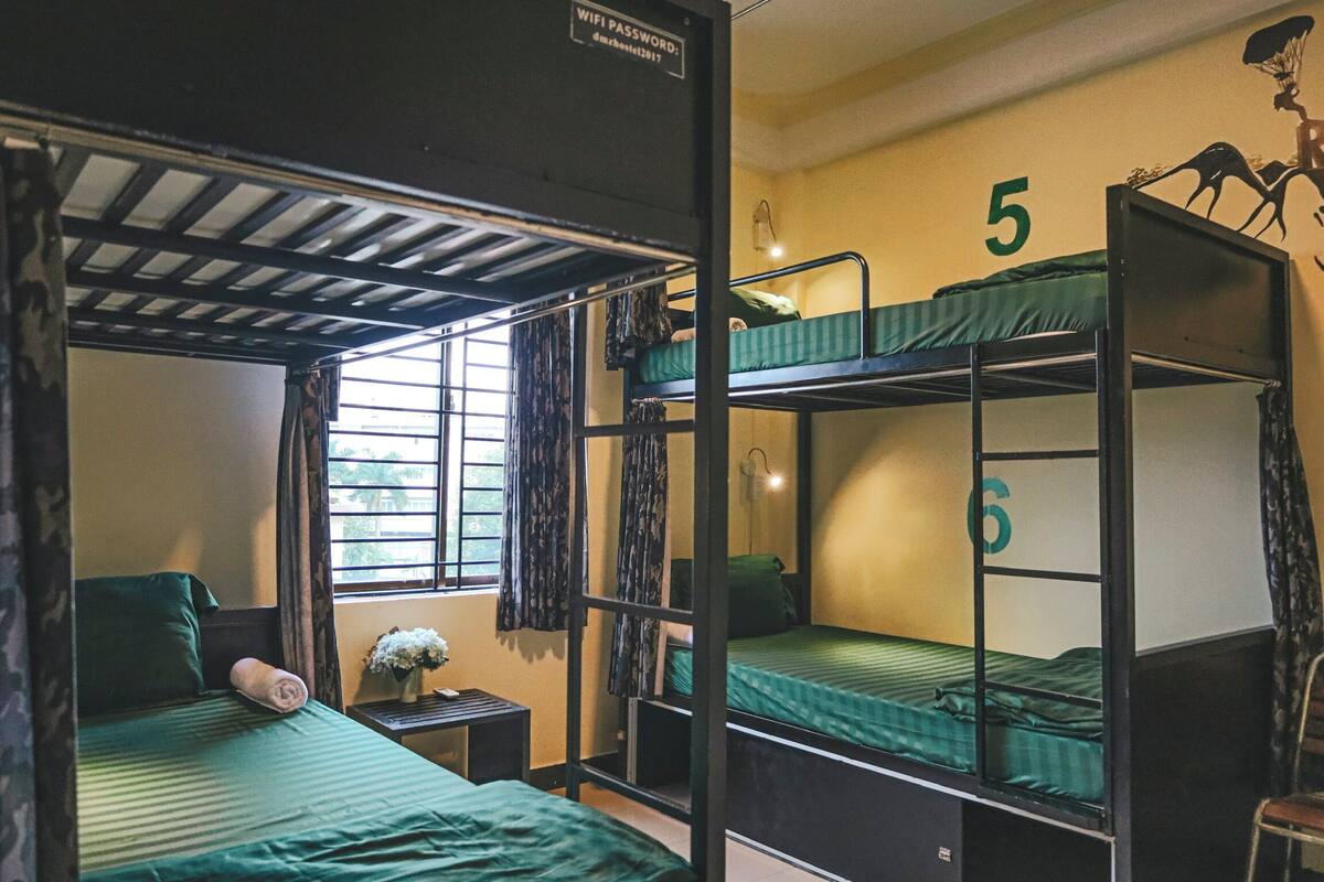 Habitación de dormitorio con literas, números 5 y 6, una mesita con un florero y una ventana con cortinas.