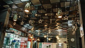 Vestíbulo de hotel con una estructura en el techo, lámparas colgantes con forma de estrella, un letrero de oficina de reservas y un ventilador.