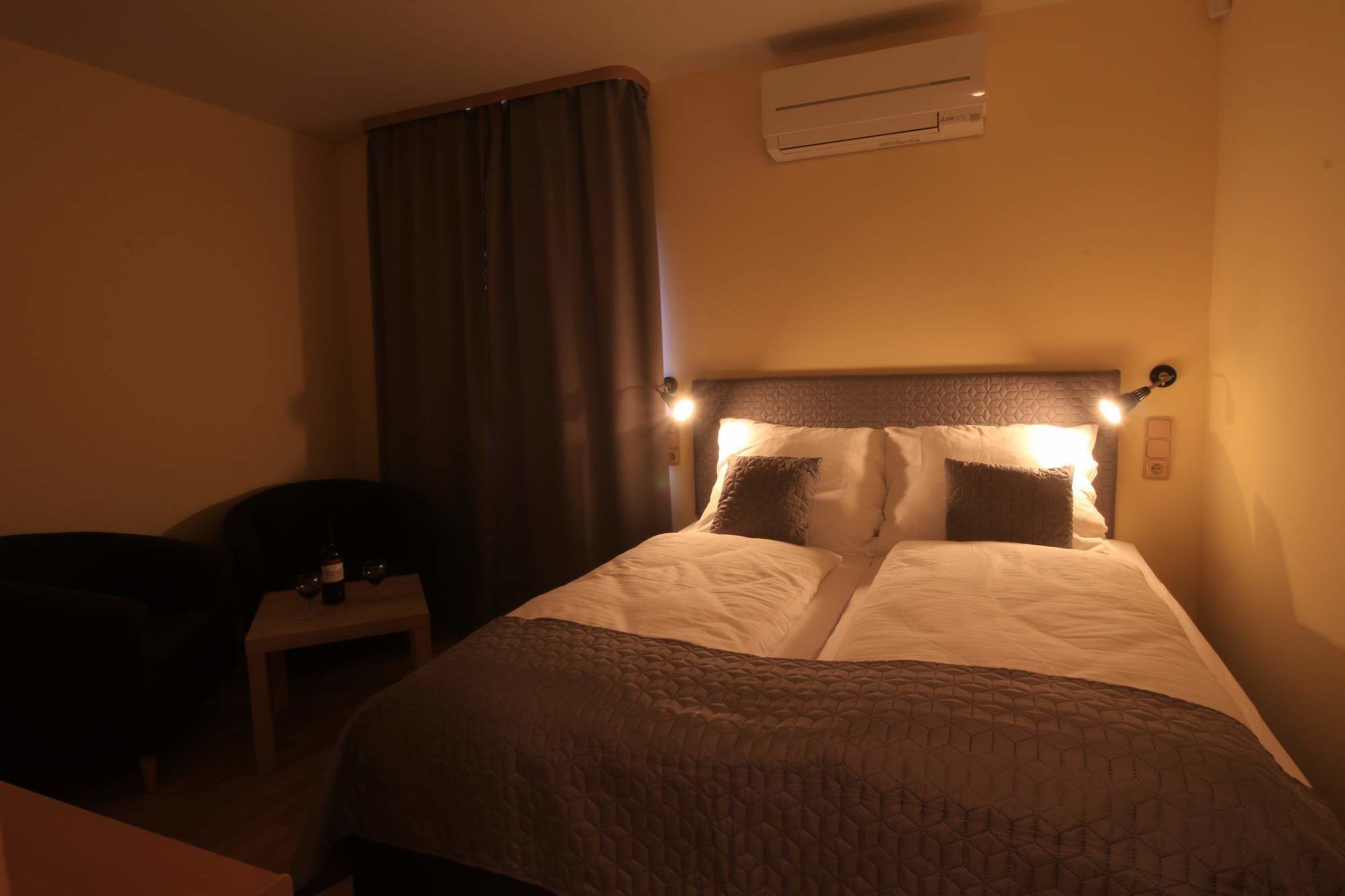 Een hotelkamer met een bed, nachtkastje, stoel en een airconditioner.