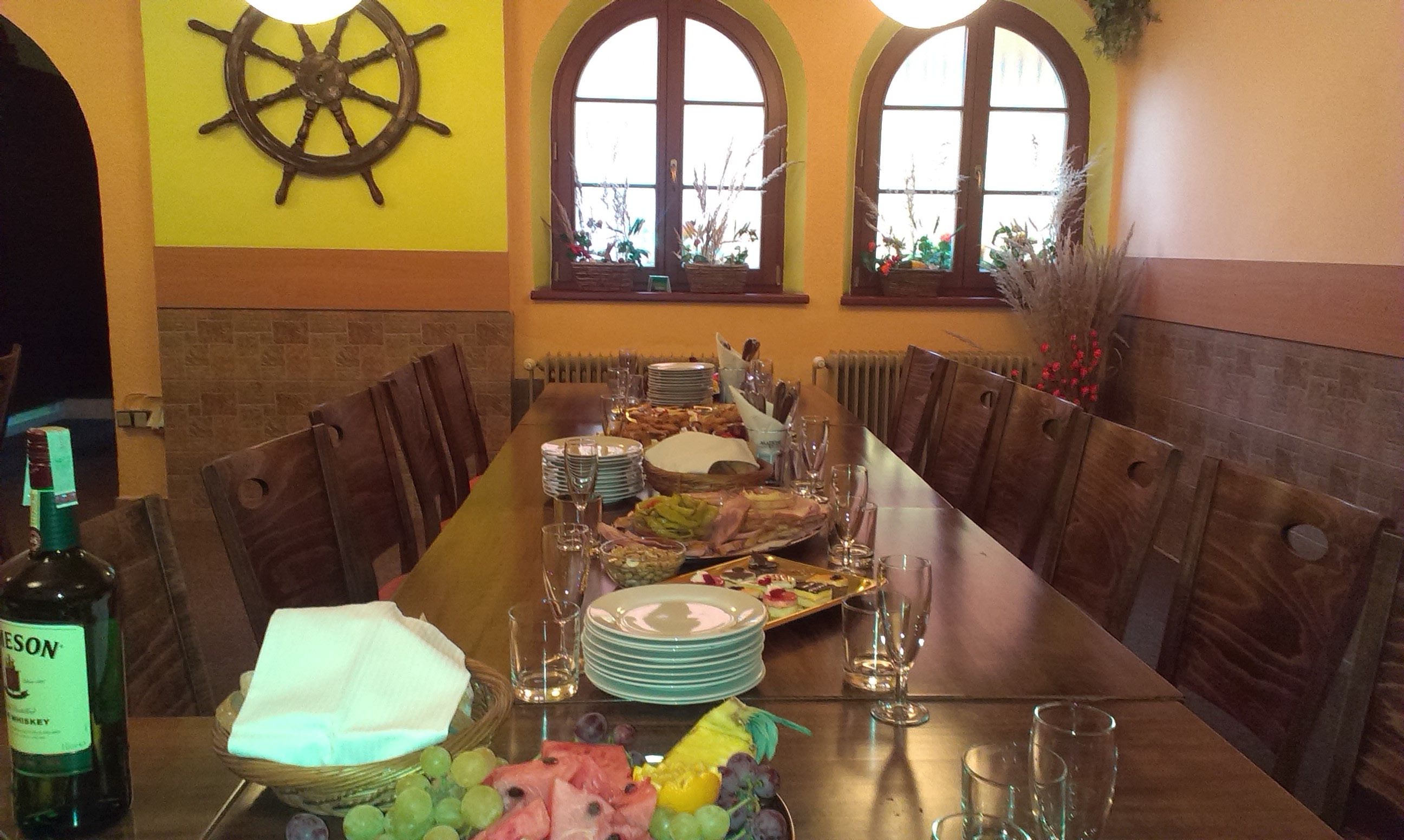 A long dining table set for a meal with plates, glasses, and a bottle of whiskey.