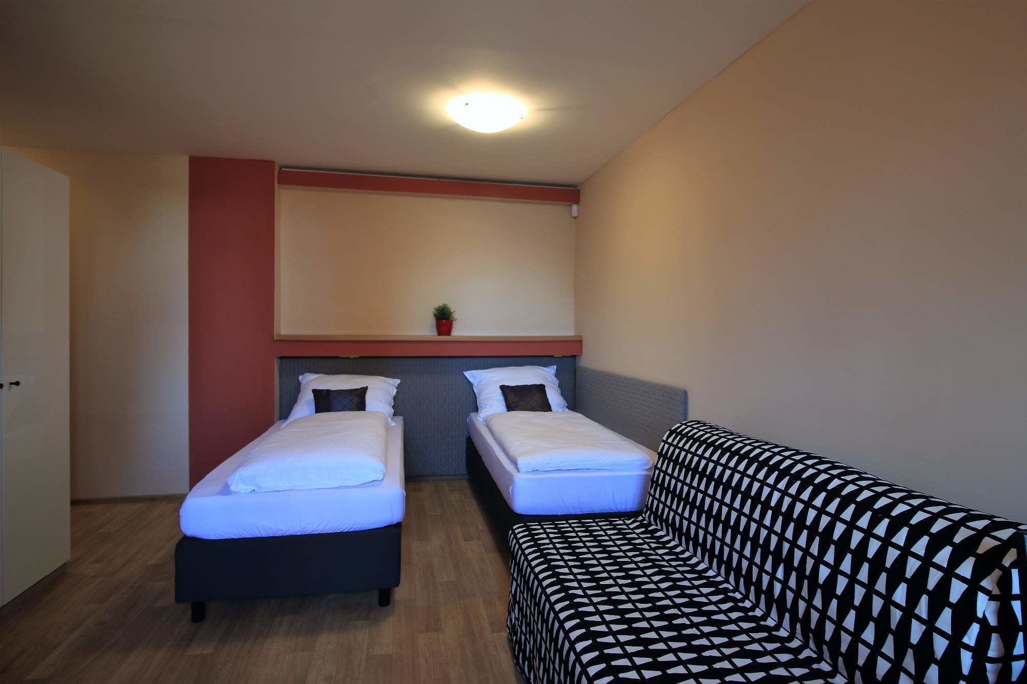 Une chambre avec deux lits simples, un canapé, une petite plante en pot et un luminaire au plafond.