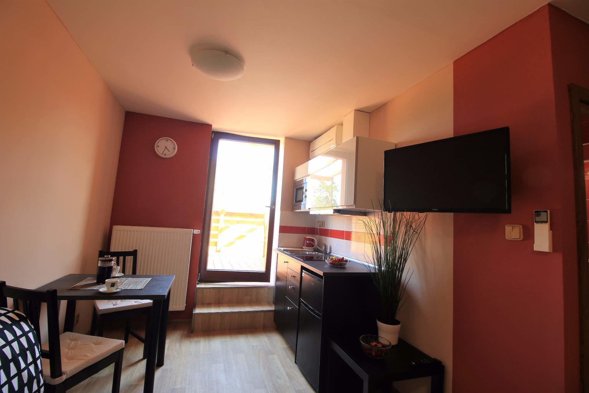 A compact kitchen with a microwave, stove, and a flat-screen TV mounted above the counter.