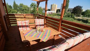 A wooden deck with a table and benches, featuring plaid cushions and a colorful tablecloth. - Penzion U Admirála (Kladno)