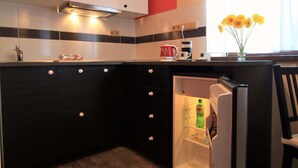 A compact kitchen with a microwave, a refrigerator, and a window with curtains. - Penzion U Admirála (Kladno)