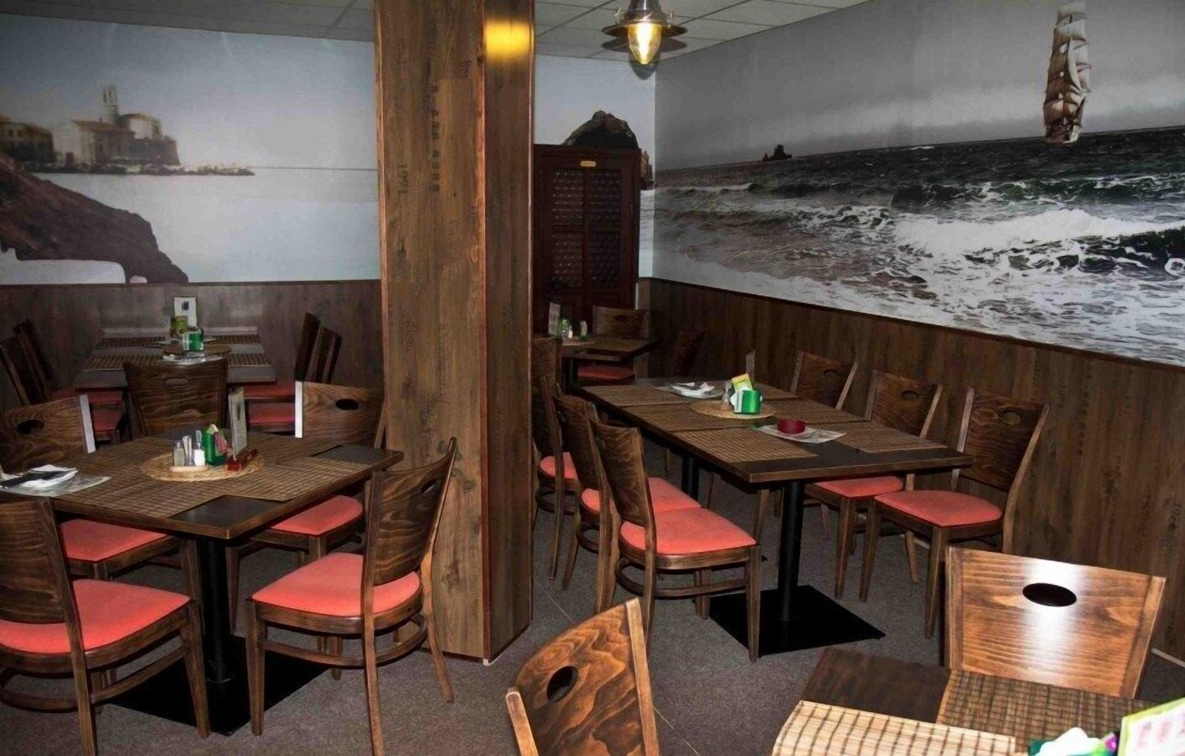 A restaurant with wooden tables and chairs, a mural of a beach scene, and a view of the ocean.