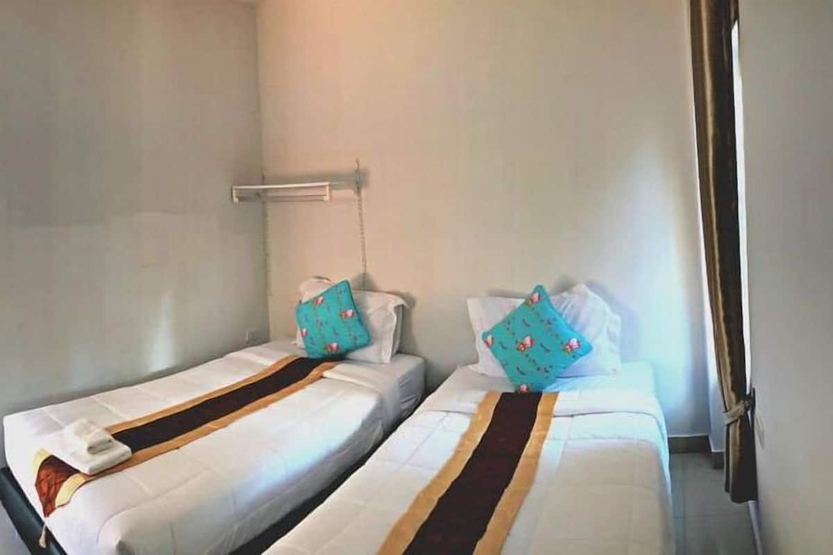 Two twin beds with matching headboards and pillows, a small bedside table, and a window with curtains.