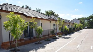 A row of residential-style buildings with tiled roofs, a parking lot, and small trees along the sidewalk. - The Wish Residence (Udon Thani)
