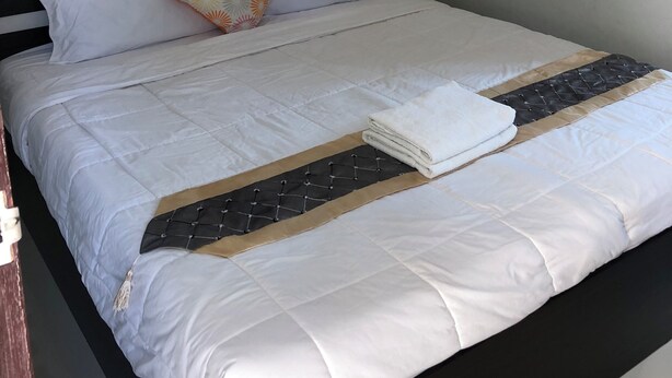 A neatly made bed with white bedding, a patterned pillow, and a folded towel on the side. - The Wish Residence (Udon Thani)