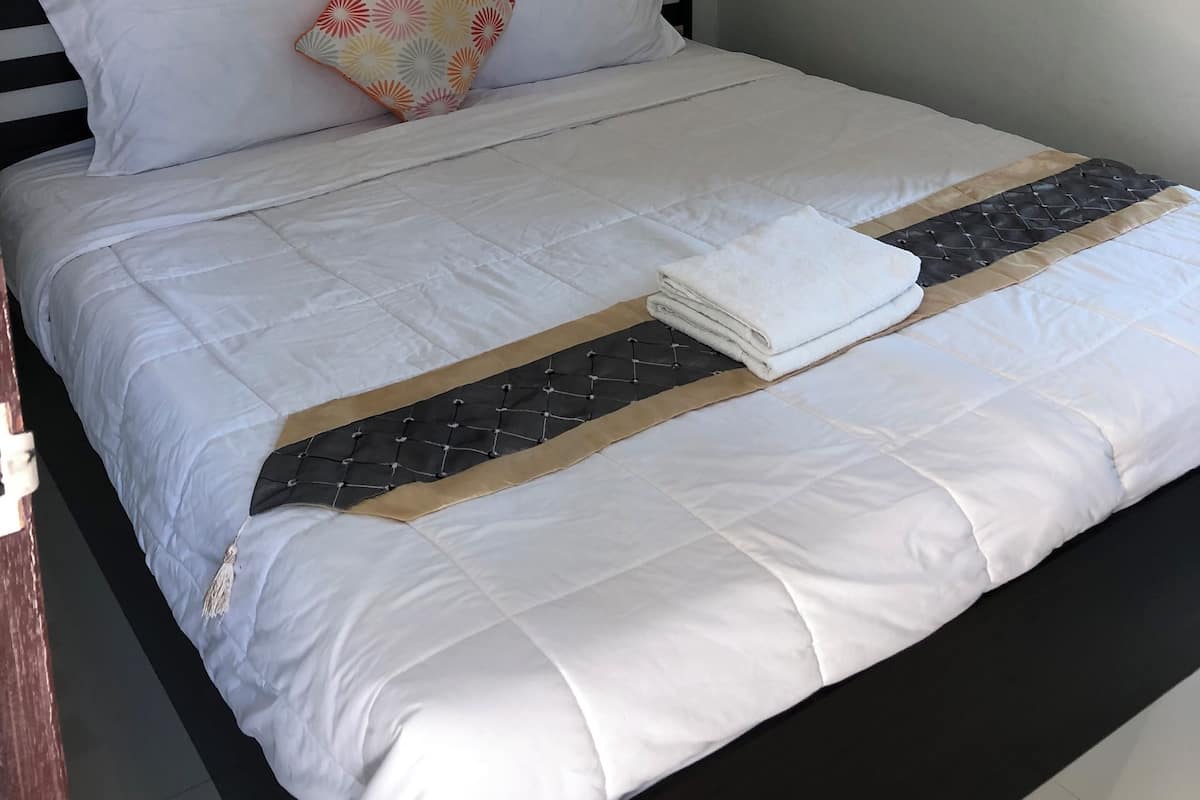 A neatly made bed with white bedding, a patterned pillow, and a folded towel on the side.