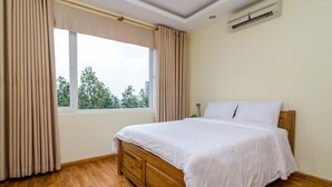 Een slaapkamer met een houten bed, beige gordijnen, een raam met uitzicht op bomen en een airconditioning aan de muur.