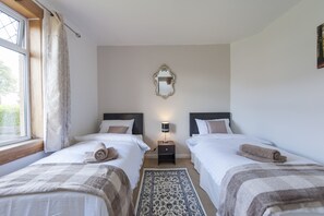 Habitación doble con dos camas, una mesita de noche con lámpara, un espejo en la pared y una ventana con cortinas.