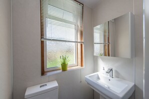 Un baño con inodoro, lavabo y ventana con persianas.