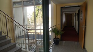 A staircase with metal railings leading to an outdoor area, a potted plant, and a hallway with a red carpet. - Apartments Aschheim (Aschheim)