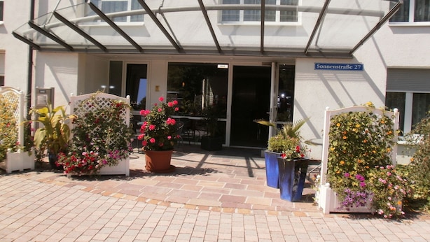 A hotel entrance with a covered patio, potted plants, and a sign indicating the street name. - Apartments Aschheim (Aschheim)