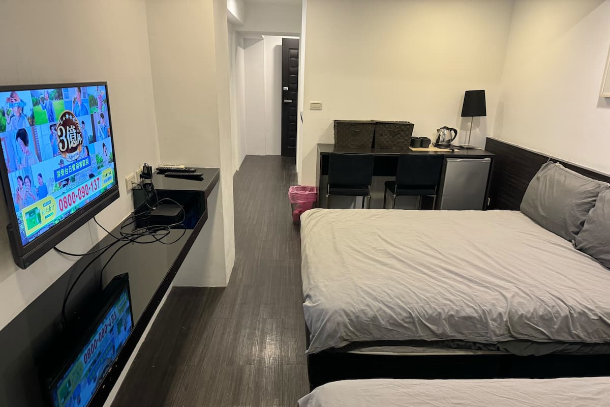 Habitación de hotel con cama, escritorio con computadora, televisor montado en la pared y pequeña zona de kitchenette.