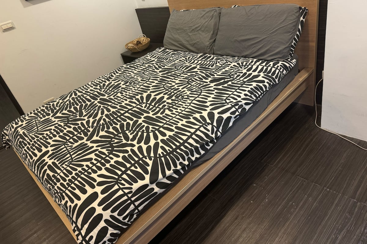 Una cama con una colcha estampada, cabecera de madera y almohada gris.