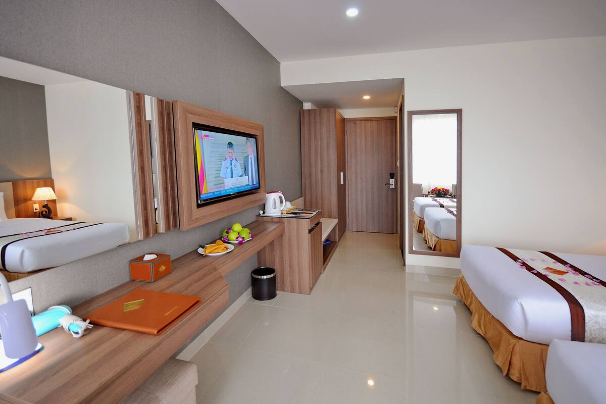 Una habitación de hotel con una cama, un escritorio con una computadora portátil, un televisor y un espejo.