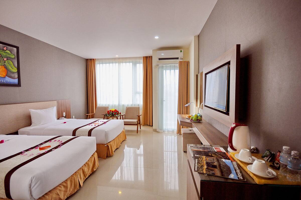 Habitación de hotel con dos camas, un escritorio con televisor, cafetera y ventana con cortinas.