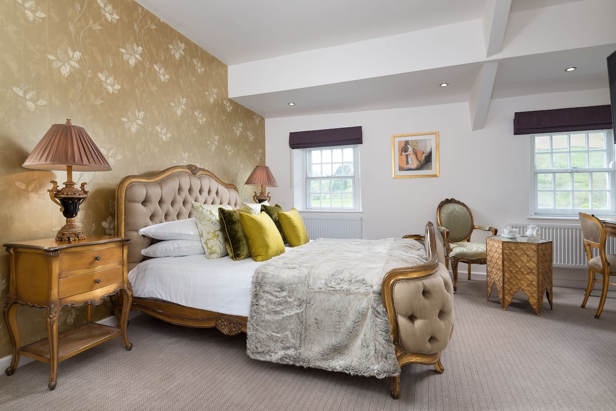 A bedroom with a large bed, a nightstand, a chair, a small table, and a window.