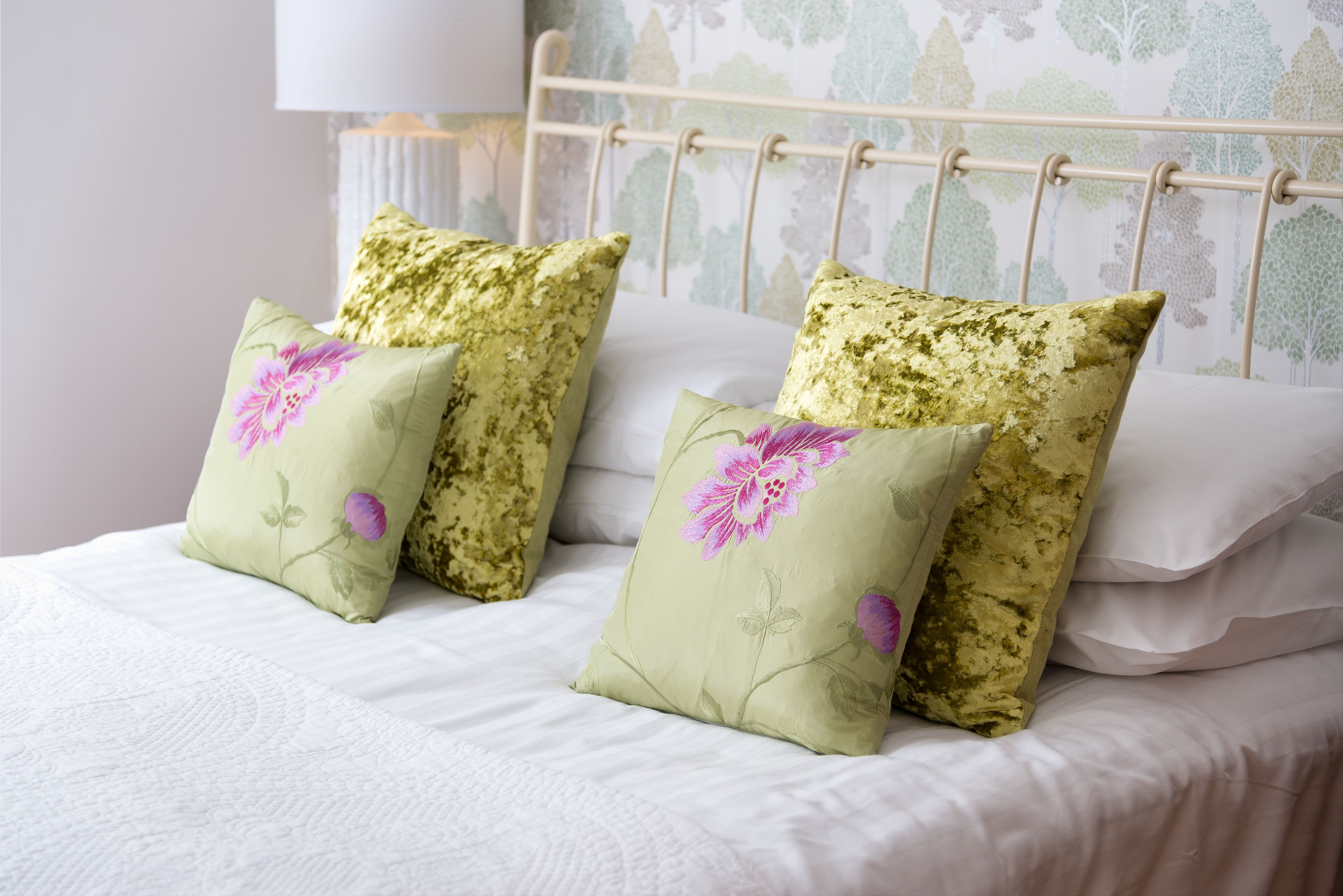 Una cama con almohadas estampadas con motivos florales y un cabecero blanco.