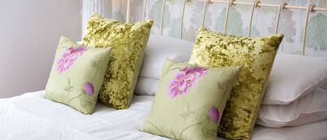Una cama con almohadas estampadas con motivos florales y un cabecero blanco.