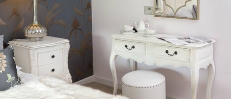A bedroom with a white vanity, a fluffy white bedspread, and a decorative lamp.