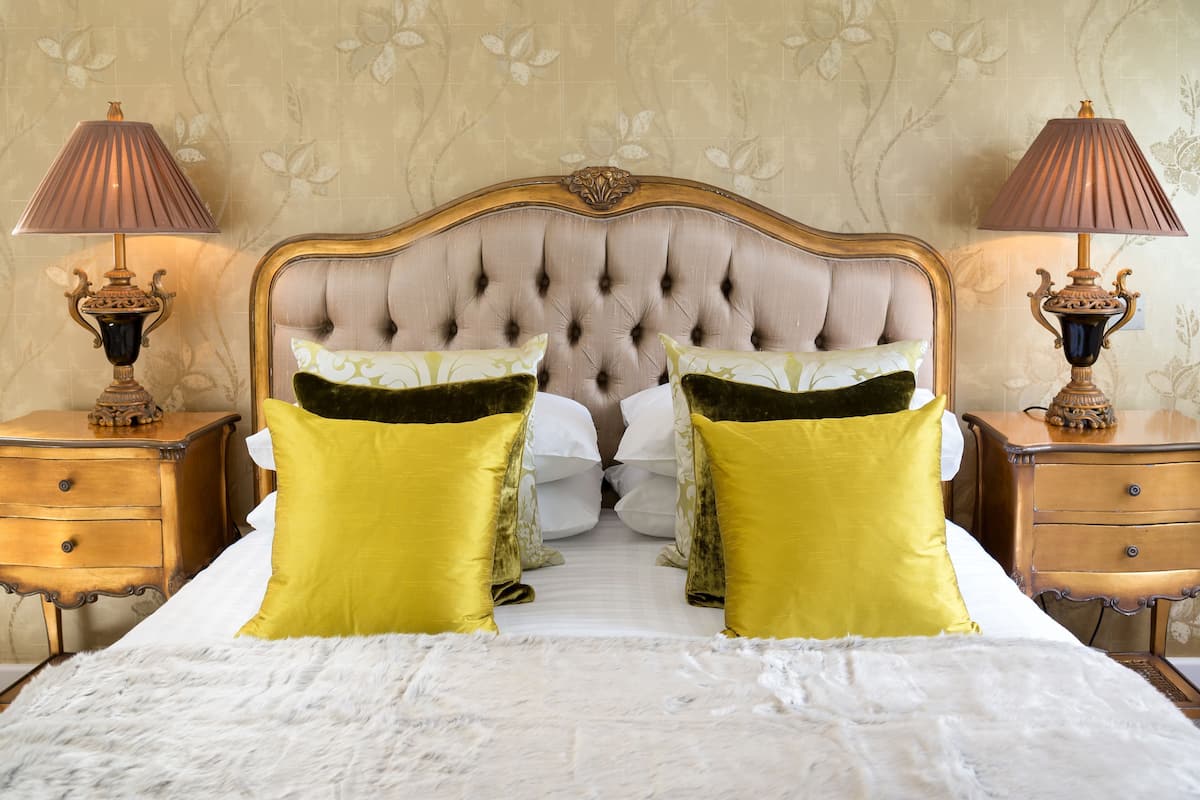A bed with a tufted headboard, two nightstands with lamps, and a floral wallpaper pattern.